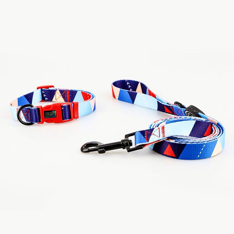 Bright geometrical dog collar and leash set, with different shades of blue being the primary colours of the set with small red triangles and white accents, black metal D rings and 360 degree swivel snap hook and a red quick release buckle for safety. Name of set is Debbie